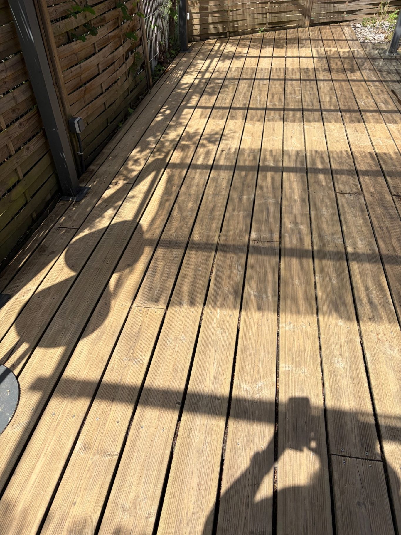 Terrasse en bois après Ombres d'un balcon en bois avec des barres et des plantes en arrière-plan.