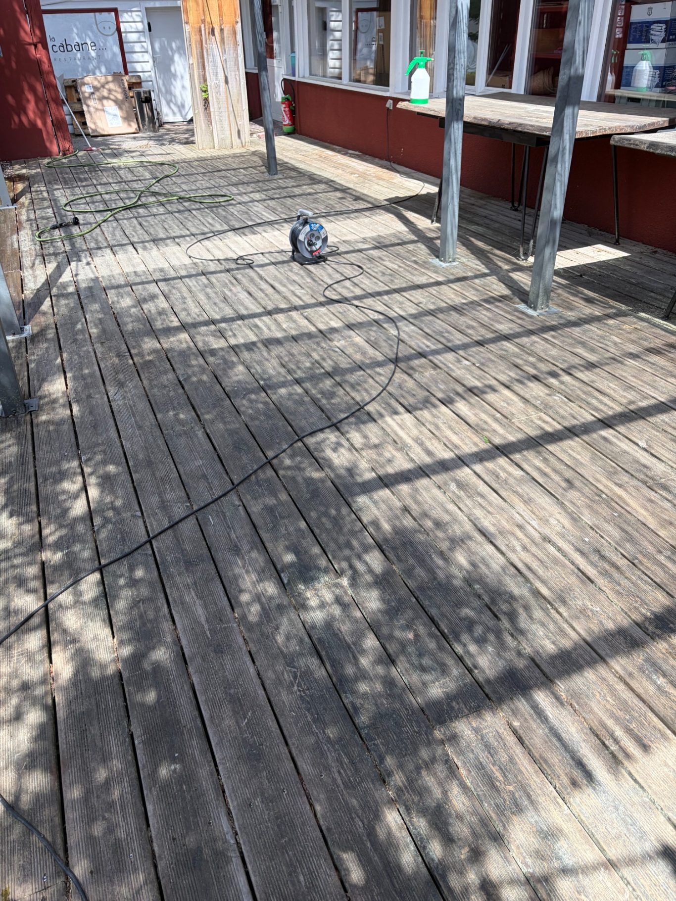 Terrasse bois avant Un chat gris se déplace sur un sol en bois, avec des ombres projetées.